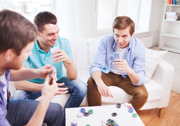 Foto lazer, jogos, amizade, jogos de azar e entretenimento - três amigos sorridentes jogando cartas em casa