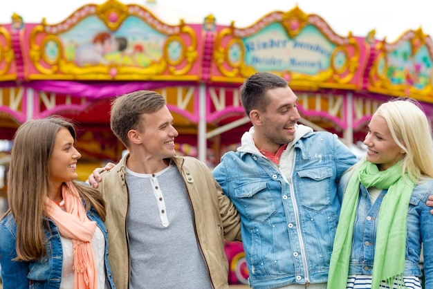 Foto lazer, parque de diversões e conceito de amizade - grupo de amigos sorridentes com carrossel nas costas