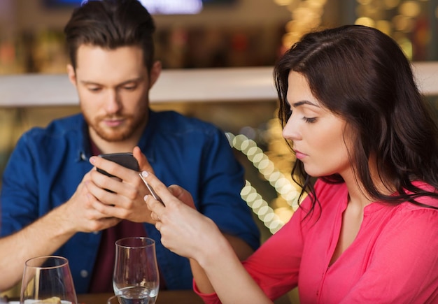 lazer, tecnologia, estilo de vida e conceito de pessoas - casal com smartphones jantando no restaurante