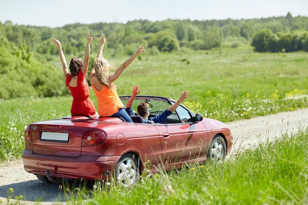 lazer, viagem, viagens e conceito de pessoas - amigos felizes dirigindo em carro cabriolet no país e acenando as mãos