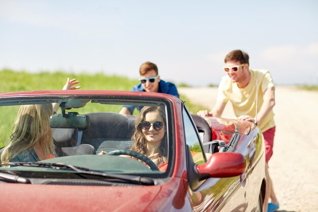 lazer, viagem, viagens e conceito de pessoas - amigos felizes empurrando carro cabriolet quebrado ao longo da estrada rural