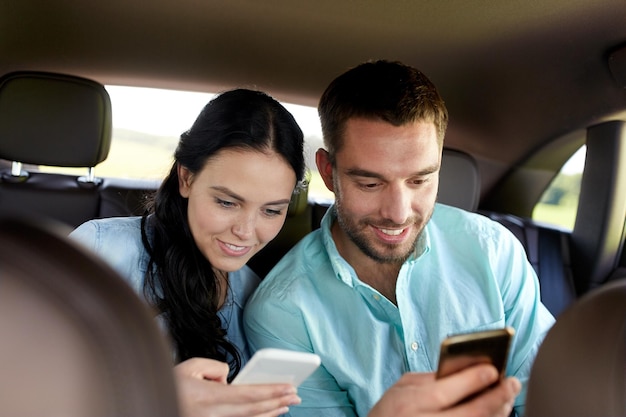 Foto lazer, viagem, viagens, tecnologia e conceito de pessoas - homem e mulher felizes com smartphones dirigindo no carro