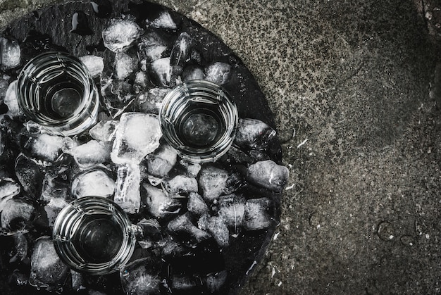 Álcool e coquetéis. Três copos de vodka em uma bandeja de ardósia, com gelo. Em uma mesa de pedra preta, copie o espaço vista superior