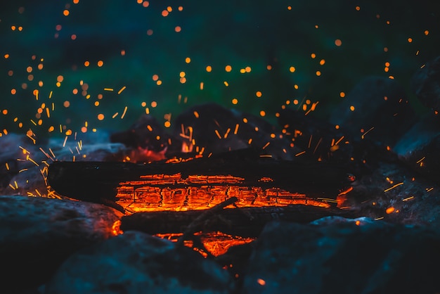 Lebendig schwelendes Brennholz brannte in Feuernahaufnahme. Atmosphärisch mit orange Flamme des Lagerfeuers. Wunderbares Vollbild des Freudenfeuers mit glühender Glut in der Luft. Warme Baumstämme, helles Funkenbokeh