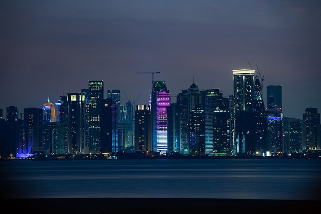 Lebendige Skyline von Doha bei Nacht von der gegenüberliegenden Seite des Sonnenuntergangs in der Hauptstadtbucht aus gesehen.