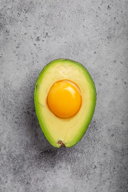 Lebensmittel, die reich an gesunden Fetten für eine ausgewogene Ernährung sind: rohes Eigelb in frisch geschnittener halber Avocado auf grauem Steinhintergrund. Ketogene Low-Carb-Diät oder Clean-Eating-Konzept, Draufsicht top