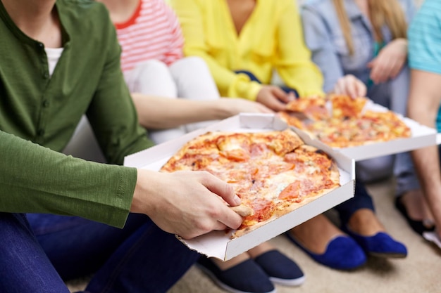 Lebensmittel-, Freizeit- und Freundschaftskonzept - Nahaufnahme glücklicher Teenager-Freunde, die zu Hause Pizza essen