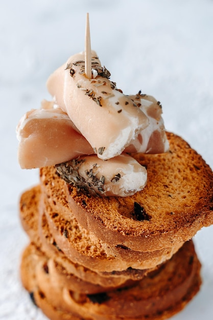 Lebensmittel-Hintergrund Ein Turm aus knusprigem Toast mit Oliven und Schinken und Frischkäse-Häppchen auf einem strukturierten, eleganten weißen Hintergrund Knuspriger Toast zum Frühstückssnack