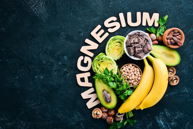 Lebensmittel mit natürlichem Magnesium Mg Schokolade Banane Kakaonüsse Avocados Brokkoli Mandeln Draufsicht Auf schwarzem Hintergrund