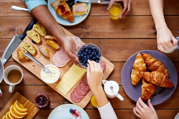 Lebensmittelessen und Familienkonzept Gruppe von Menschen, die bei einem Holztisch Blaubeeren zum Frühstück teilen