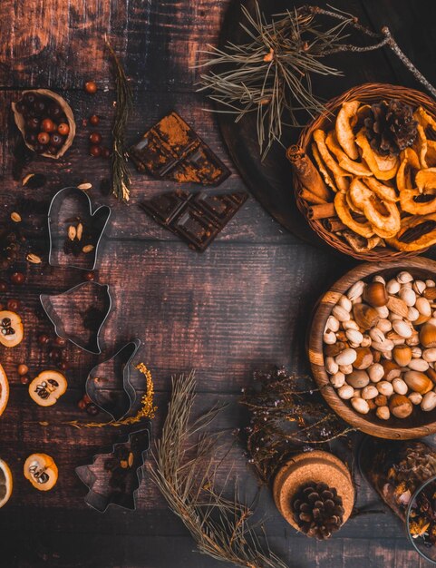 Lebensmittelhintergrund mit weihnachtlichen Gewürzen, getrockneten Äpfeln, Nüssen, Zitrusfrüchten, Cydonia, Preiselbeeren, Rosinen und Auflaufform auf Holzhintergrund, Ansicht von oben mit Kopierraum