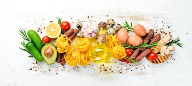 Lebensmittelhintergrund Trockene Nudeln, Tomaten, Gewürze und Gemüse auf einem weißen Holzhintergrund Draufsicht