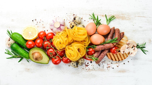 Lebensmittelhintergrund Trockene Nudeln, Tomaten, Gewürze und Gemüse auf einem weißen Holzhintergrund Draufsicht
