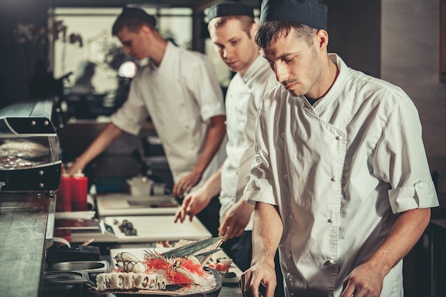 Foto lebensmittelkonzept drei junge köche in weißer uniform dekorieren fertiggerichte im restaurant, in dem sie arbeiten