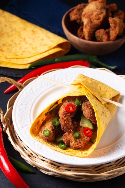 Lebensmittelkonzept würziger Fried Chicken Tortilla Wrap mit gehackten Chilis auf schwarzem Schiefersteinhintergrund mit Kopierraum