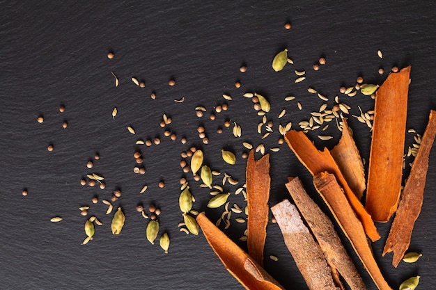 Lebensmittelkonzeptzusammenstellung Orientalische Gewürzkardamomhülsen, Koriandersamen, Fenchel und Zimt Cassia Bark Sticks auf schwarzem Schiefer