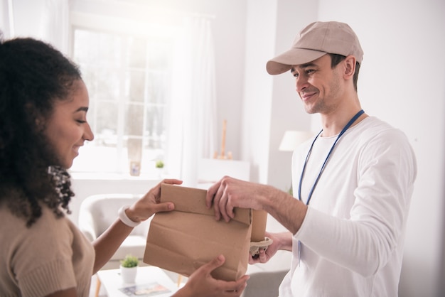 Lebensmittellieferservice. Glückliche nette Person, die die Tasche nimmt, während sie den Lieferboten ansieht