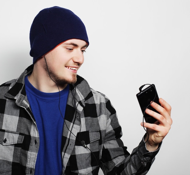 Lebensstil, Bildung und Menschenkonzept: junger Mann, der Musik hört und Smartphone benutzt, während er vor grauem Hintergrund steht.