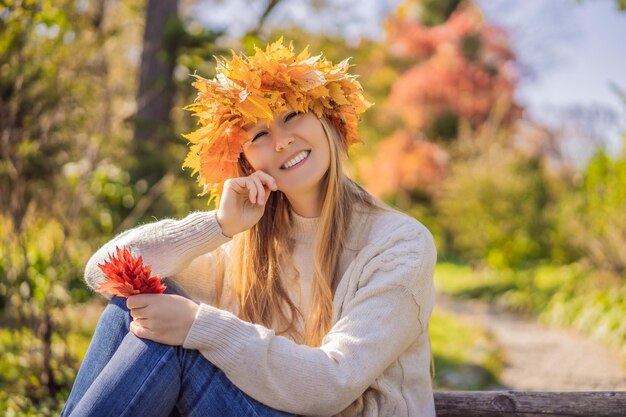 Foto lebensstil im freien nahaufnahme porträt einer charmanten blonden jungen frau, die einen kranz aus herbstblättern trägt. sie trägt einen stilvollen strickpullover. kranz aus ahornblättern