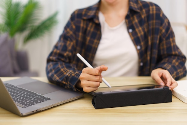 Lebensstil im Wohnzimmerkonzept Junge asiatische Frau, die einen Laptop verwendet und Daten auf dem Tablet notiert