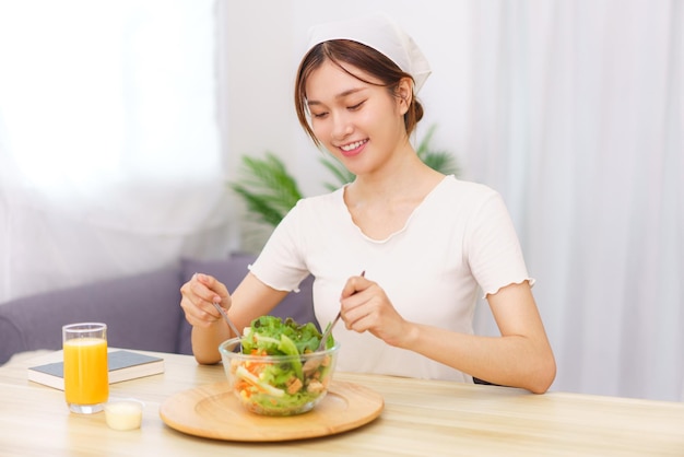 Lebensstil im Wohnzimmerkonzept Junge asiatische Frau, die zum Frühstück Gemüsesalat in einer Schüssel mischt