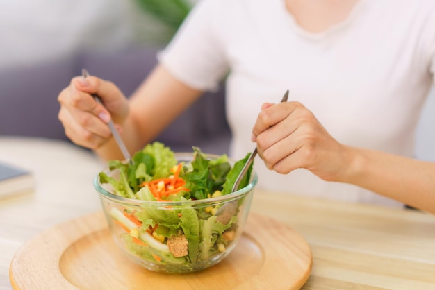 Lebensstil im Wohnzimmerkonzept Junge asiatische Frau, die zum Frühstück Gemüsesalat in einer Schüssel mischt