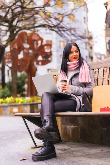 Lebensstil, kaukasisches brünettes Mädchen, das mit Laptop in einem Park arbeitet, sitzt auf einer Bank