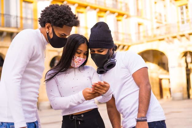 Lebensstil, Latino-Freunde, die Spaß mit Gesichtsmasken haben, die etwas am Telefon betrachten.