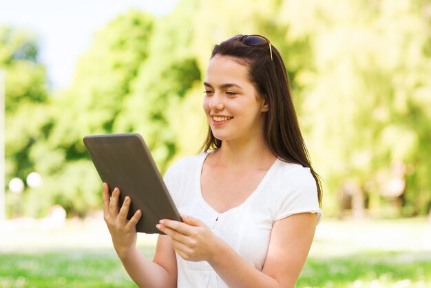 Lebensstil, Sommer, Urlaub, Technologie und Personenkonzept - lächelndes junges Mädchen mit Tablet-PC-Computer, das auf Gras im Park sitzt