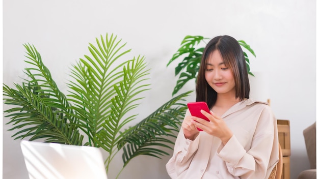 Lebensstil zu Hause Konzept Asiatische Frau, die auf einem Stuhl sitzt und mit dem Smartphone in sozialen Medien surft