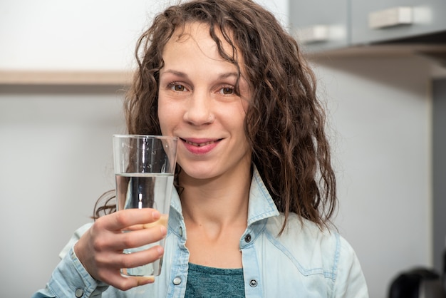 Lebensstilporträt des langhaarigen schönen Mädchens, das ein Wasser trinkt