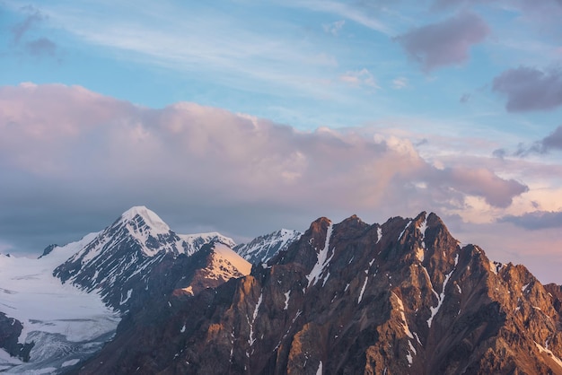 Lebhafte alpine Landschaft mit hohem schneebedeckten Felsgipfel in goldenen Sonnenaufgangsfarben. Farbenfrohe Berglandschaft mit sonnenbeschienenen goldenen Felsen und schneebedeckten Berggipfeln bei Sonnenaufgang. Früher Morgen in sehr großer Höhe