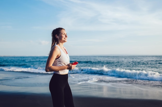 Lebhafte Frau, die am Meer Musik auf dem Smartphone hört