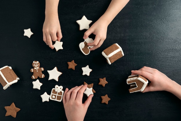 Lebkuchen hausgemachte Kekse in Kinderhänden. Süßigkeiten des neuen Jahres. Schwarzer Hintergrund.