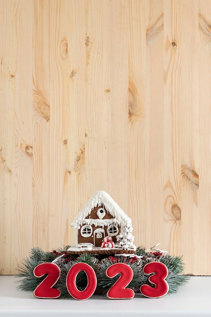 Lebkuchenhaus und Aufschrift 2023 Frohe Weihnachten Hintergrund kopieren Raum Vertikaler Rahmen Helle Holzwand im Hintergrund