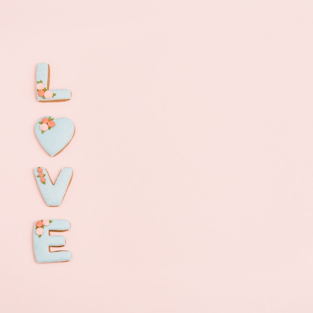 Lebkuchenherz, Kekse in Form der Buchstabenliebe mit Zuckerguss auf Pastellrosa