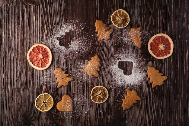 Lebkuchenplätzchen im Weihnachtstannenbaum und im Herzen formen, Puderzucker auf Holztisch, Zitrusfruchttrockenfrüchte, Draufsicht