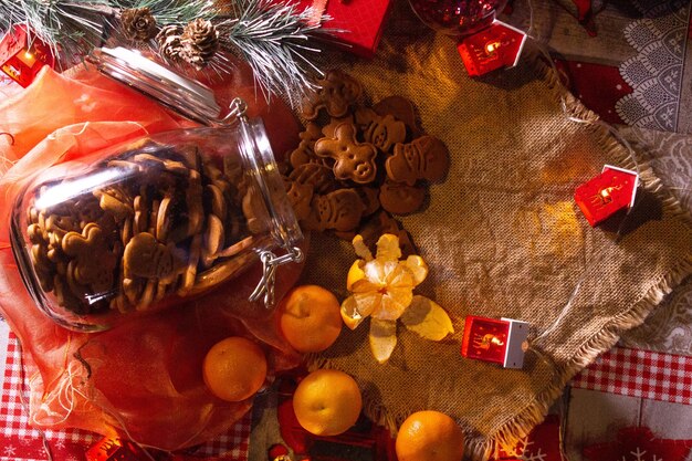 Lebkuchenplätzchen in einem Glas. Mandarinen sorgen für Neujahrsstimmung. Festliche Laternen im Vordergrund. All dies vor dem Hintergrund von Leinenmaterial.