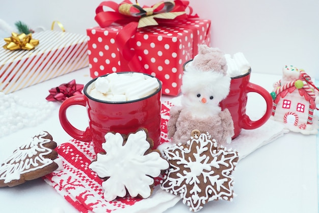 Lebkuchenplätzchen in Form einer Schneeflocke, rote Becher mit Kaffee und Eibische, Geschenkboxen, Spielzeugschneemann.