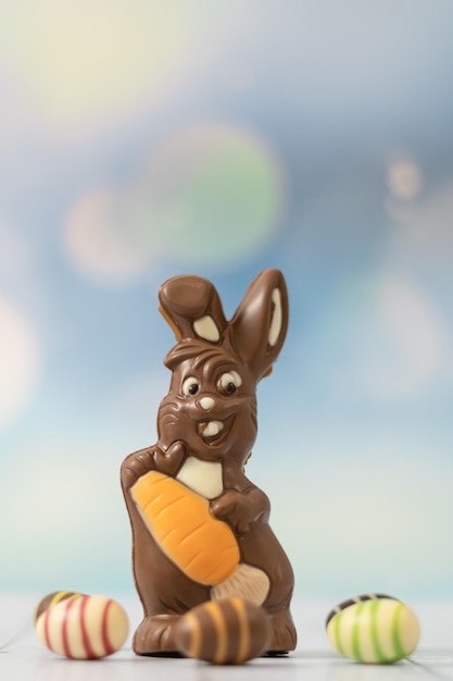 Foto lebre de chocolate com cenouras e ovos de páscoa em um fundo claro