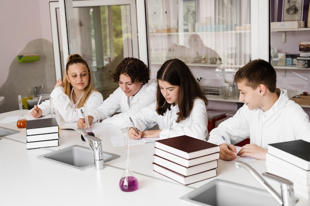 Lección de química en el laboratorio de la escuela Los alumnos escriben la tarea sonriendo y divirtiéndose juntos en el laboratorio de la escuela