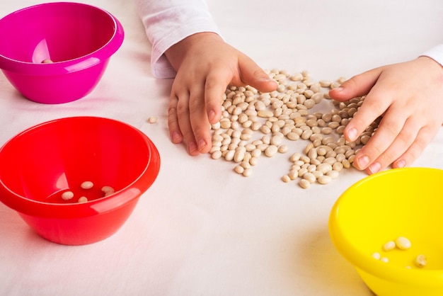 Lecciones de desarrollo para niños pequeños El desarrollo de habilidades motoras finas Frijoles blancos y recipiente de plástico de colores