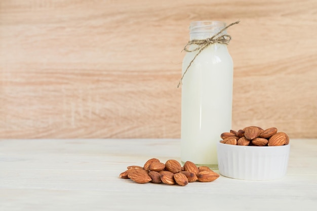 Leche de almendra casera en una botella y nueces en un cuenco de porcelana blanca sobre fondo de madera