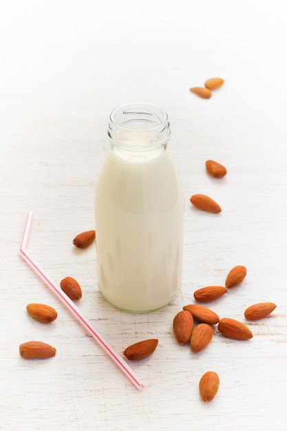 Leche de almendras en la botella, almendras y paja sobre un fondo blanco