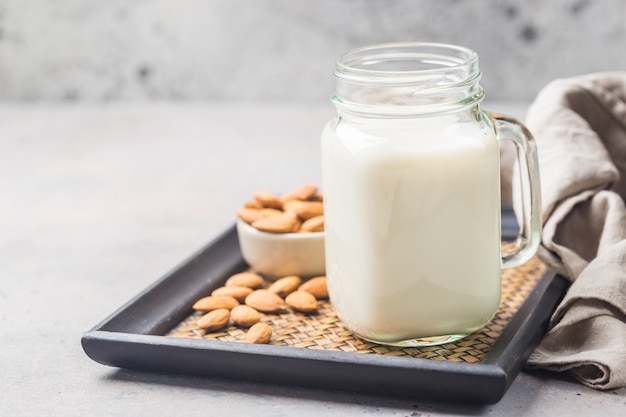 Leche de almendras orgánica en un vaso con almendras sobre una superficie gris