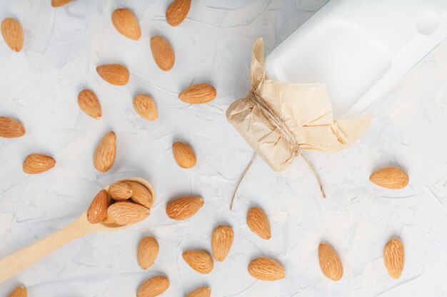 Leche de almendras orgánicas en una botella transparente con un esparcimiento de semillas y una cuchara de madera sobre un fondo claro