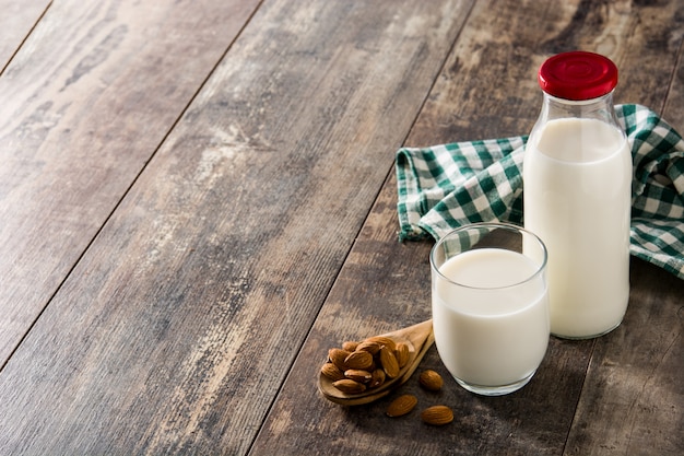 Foto leche de almendras en vidrio y botella en mesa de madera.