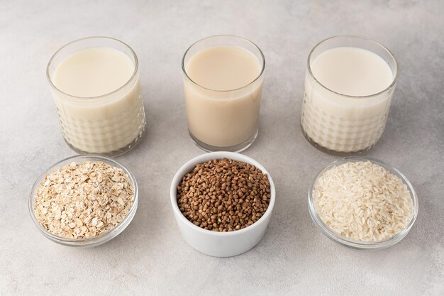 Leche alternativa en vasos de avena, arroz de trigo sarraceno y tazones con un ingrediente sobre un fondo claro