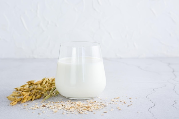 Leche de avena en orejas de vidrio y harina de avena seca esparcida sobre una mesa de luz Alimentos vegetales alternativos Espacio de copia