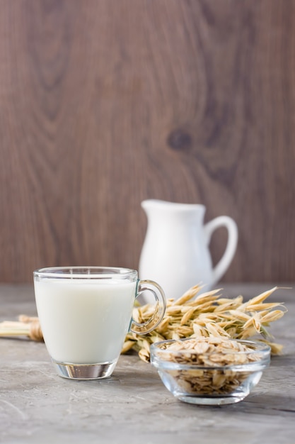 Leche de avena en una taza, avena y mazorcas de maíz en la mesa. Alternativa a la leche de vaca. Vista vertical